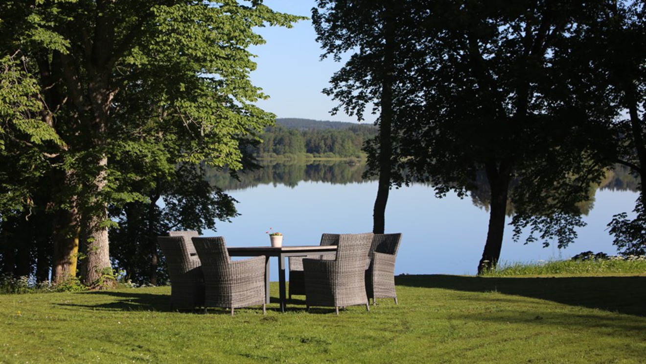 Ett loungeset med utemöbler står på gräset framför en sjö.