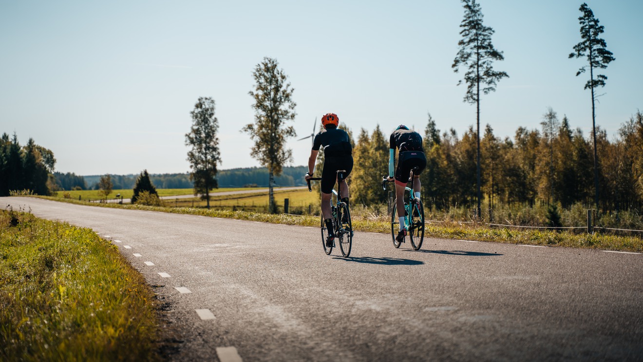 Två personer cyklar på en landsväg under blå himmel.