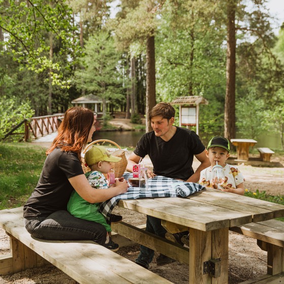 Familj sitter vid träbord och fikar i skogen.