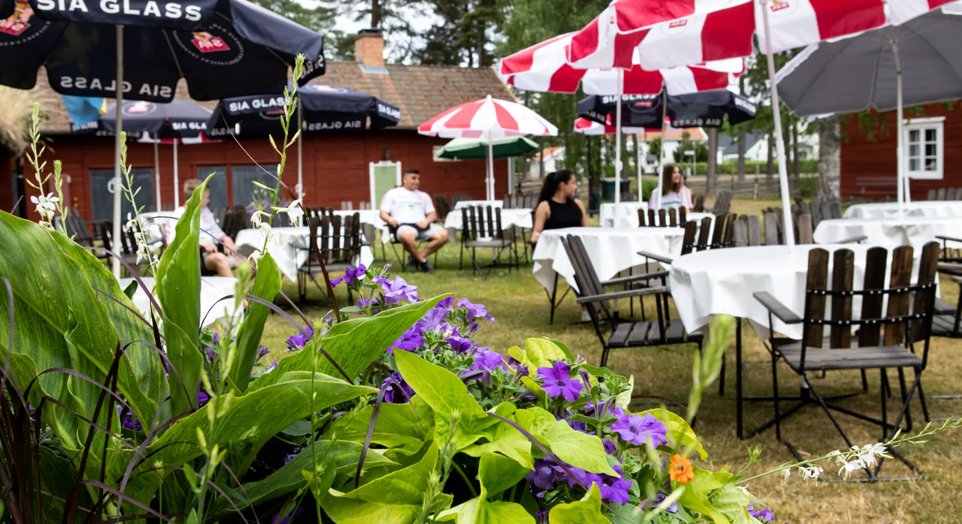 En grupp människor som sitter vid bord med parasoller över sig, caféet i forngården.