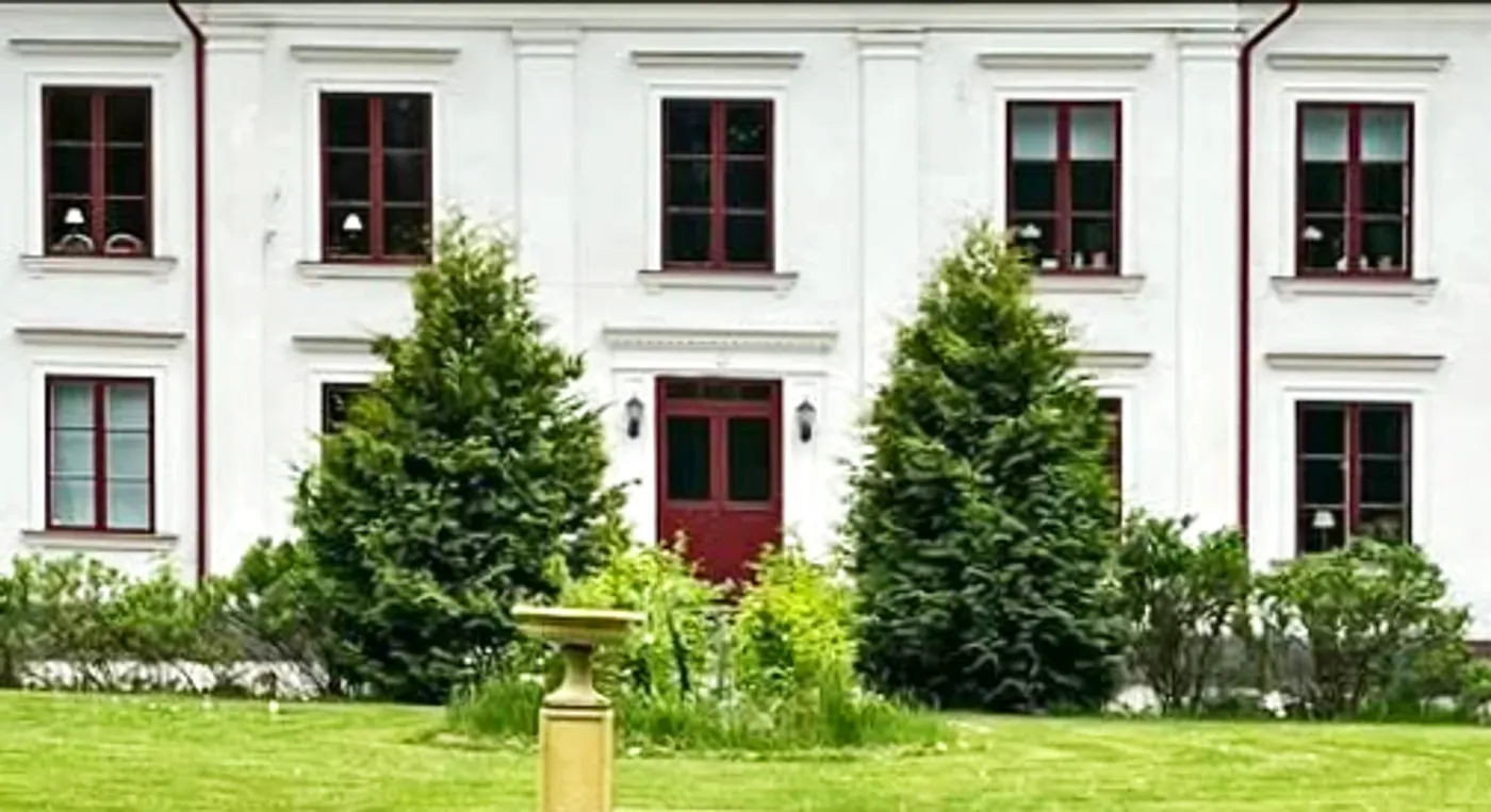 Ett gult fågelbad framför en stor vit byggnad.