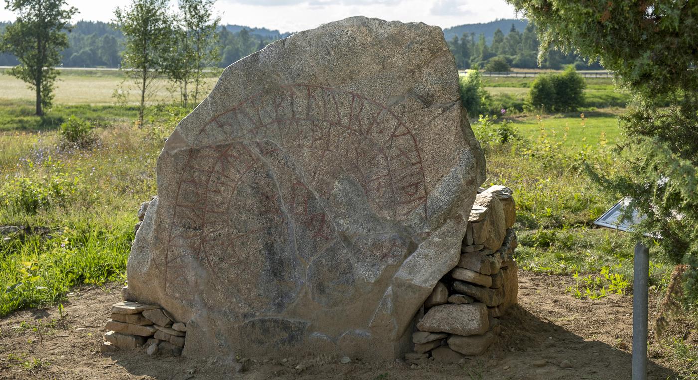 En stor runsten som står i kanten på ett fält.