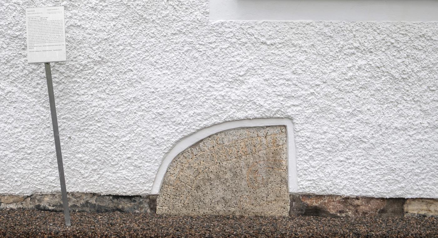 En vit byggnad med en runsten framför sig.