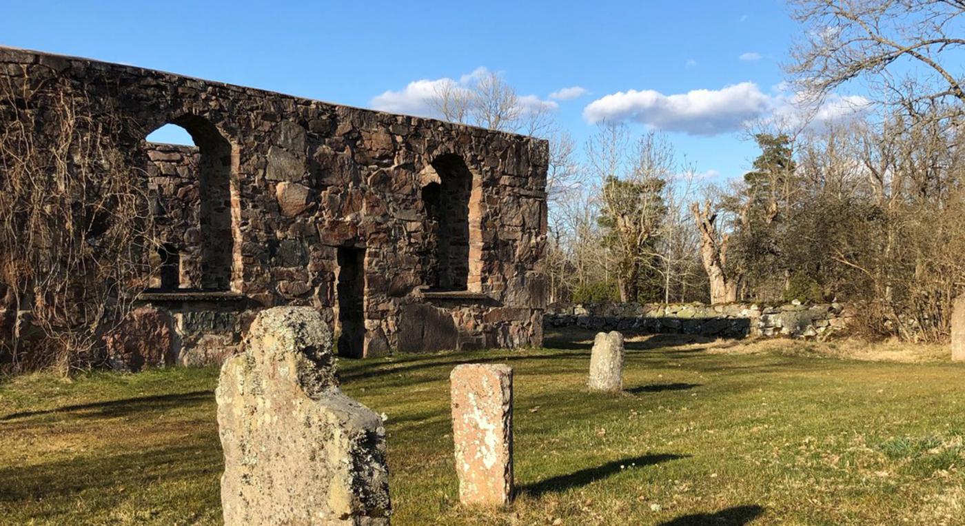 En stenruin med gamla gravstenar framför sig