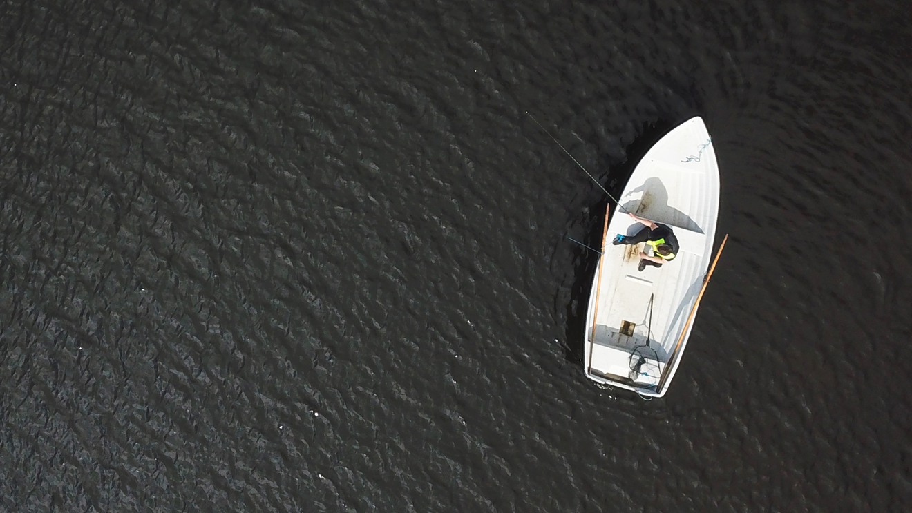 En fiskare i en båt ute på en sjö, sett ovanifrån.