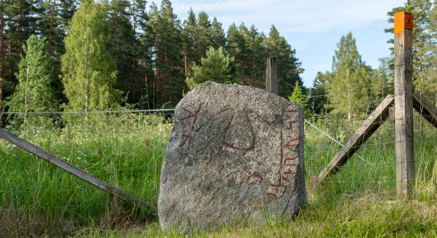 En stor runsten som ligger mitt på ett fält.