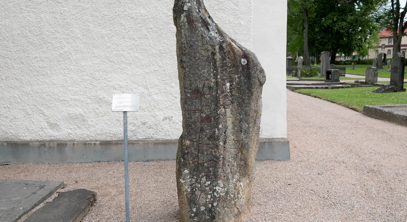 En stor runsten framför en vit kyrkbyggnad.