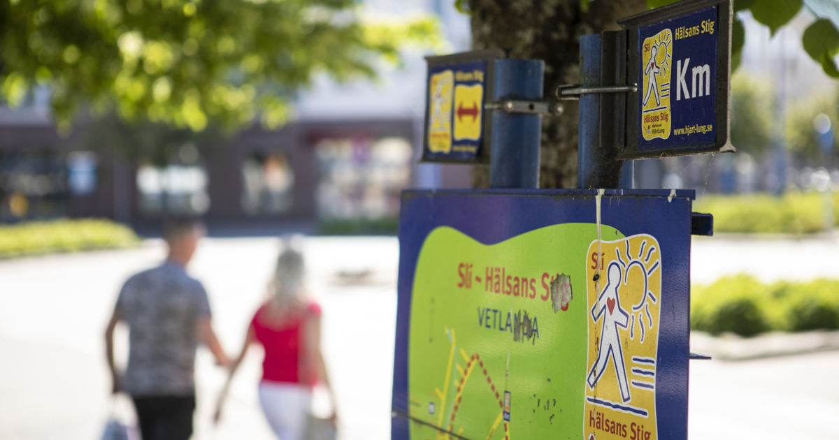 Skylt med Hälsans stig och personer som promenerar genom Vetlanda.
