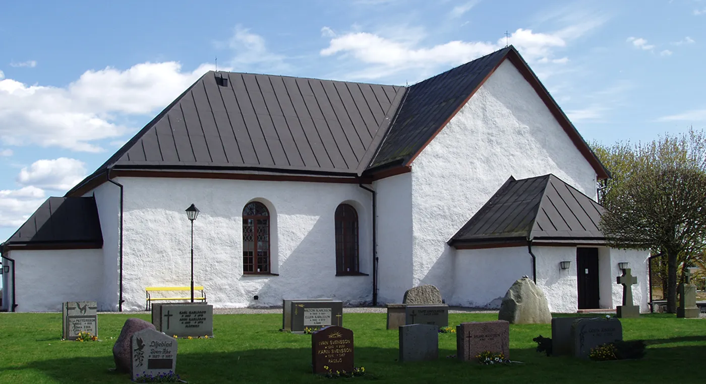 En vit kyrka med gravstenar framför sig.
