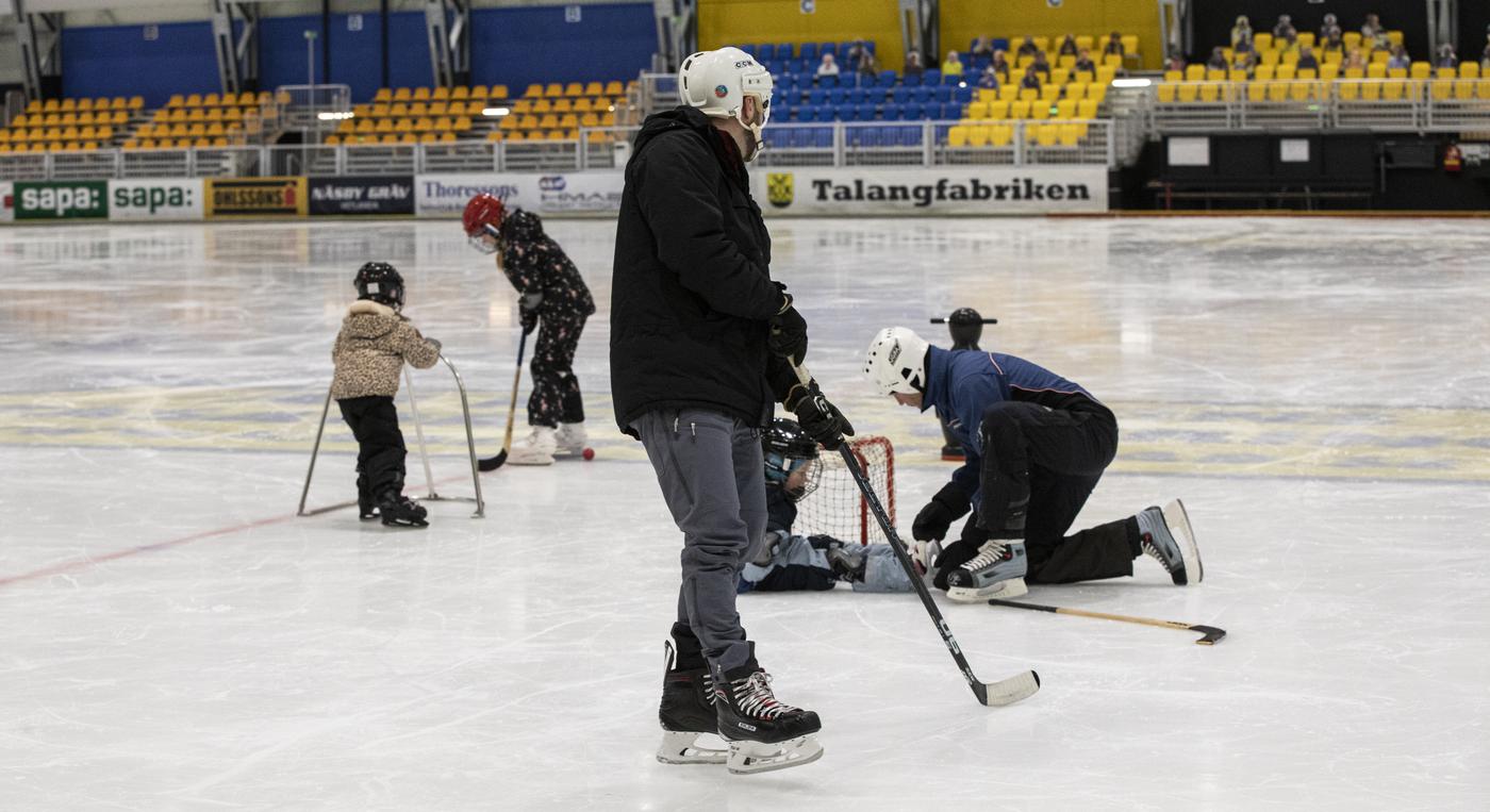 Två män och tre barn åker skridskor i en ishall.