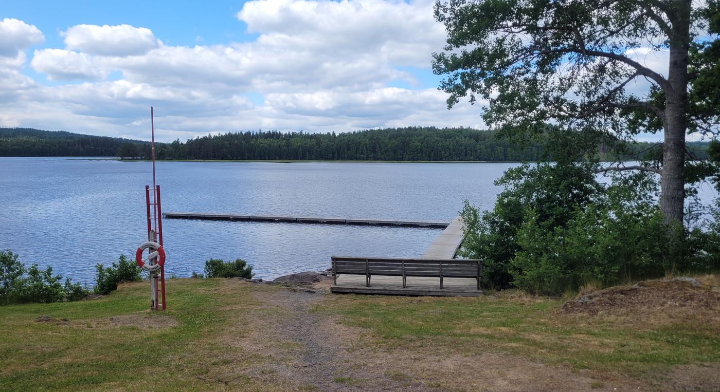 En brygga i vattnet, på land syns en lång bänk på ett litet trädäck