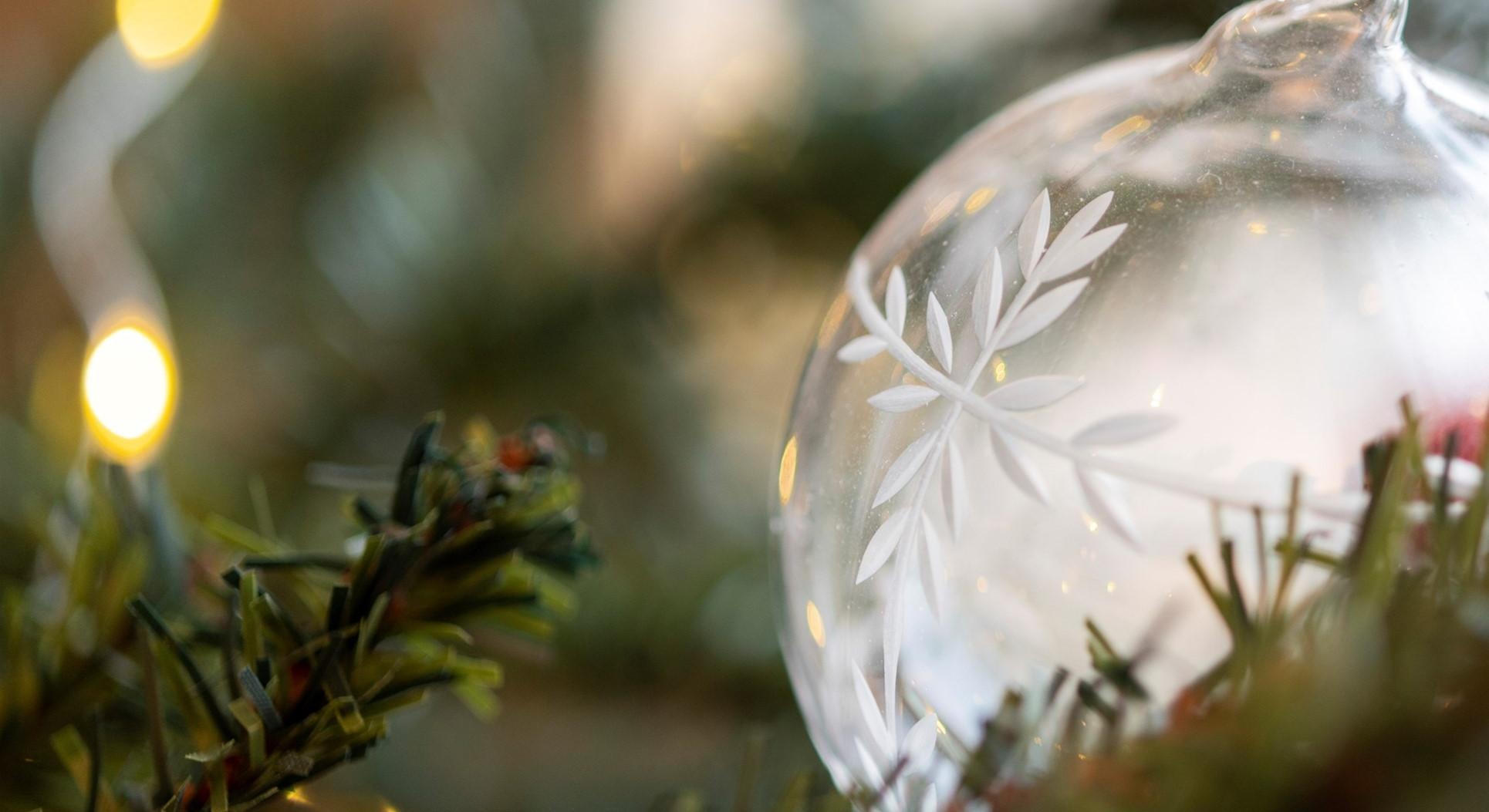 Silvrig julgranskula av glas i närbild, hänger i en gran.