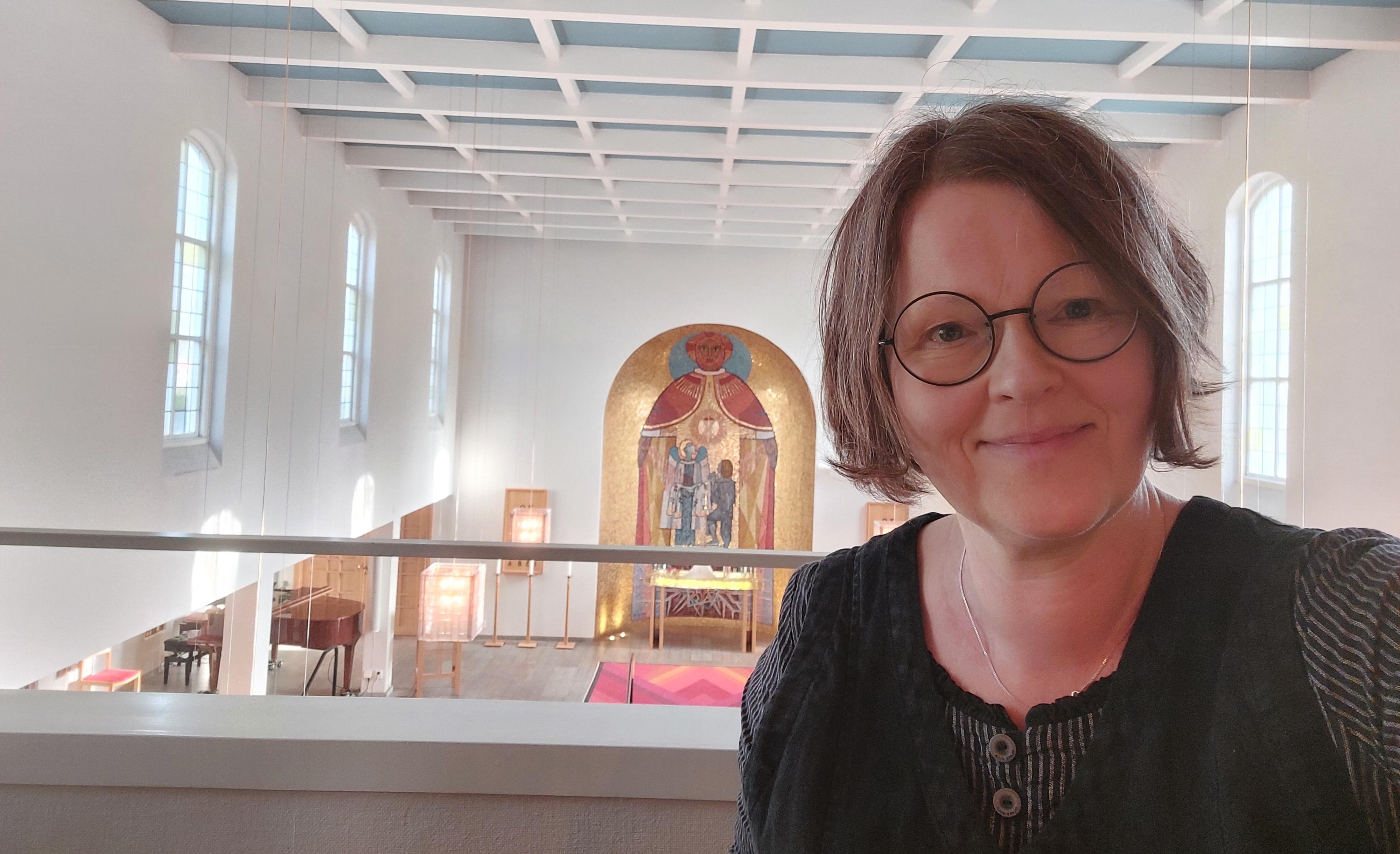 Karin tittar fram till höger i bild. Hon står uppe på en orgelläktare, så bakom henne skymtar altaret framme i en kyrka.