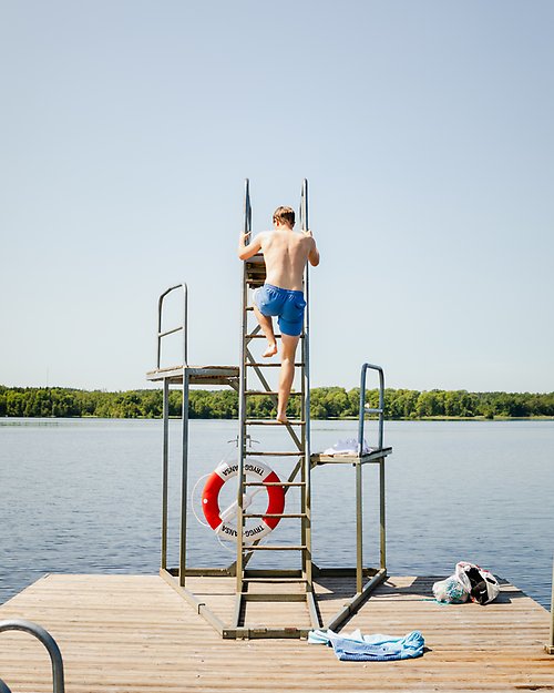 En pojke klättrar upp för ett hopptorn en solig sommardag