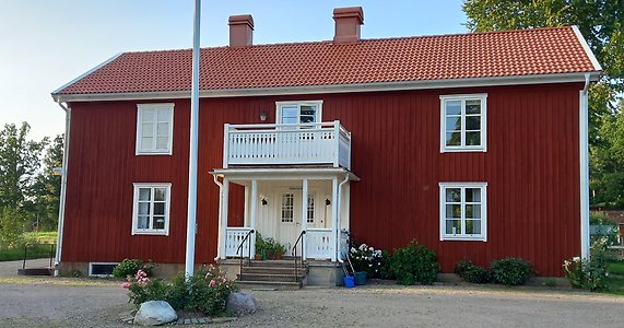 Ett rött tvåvåningshus med vita knutar och vit veranda.